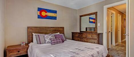 A bedroom with a wooden bed, a nightstand, a dresser, a mirror, and a wall with a flag painting.