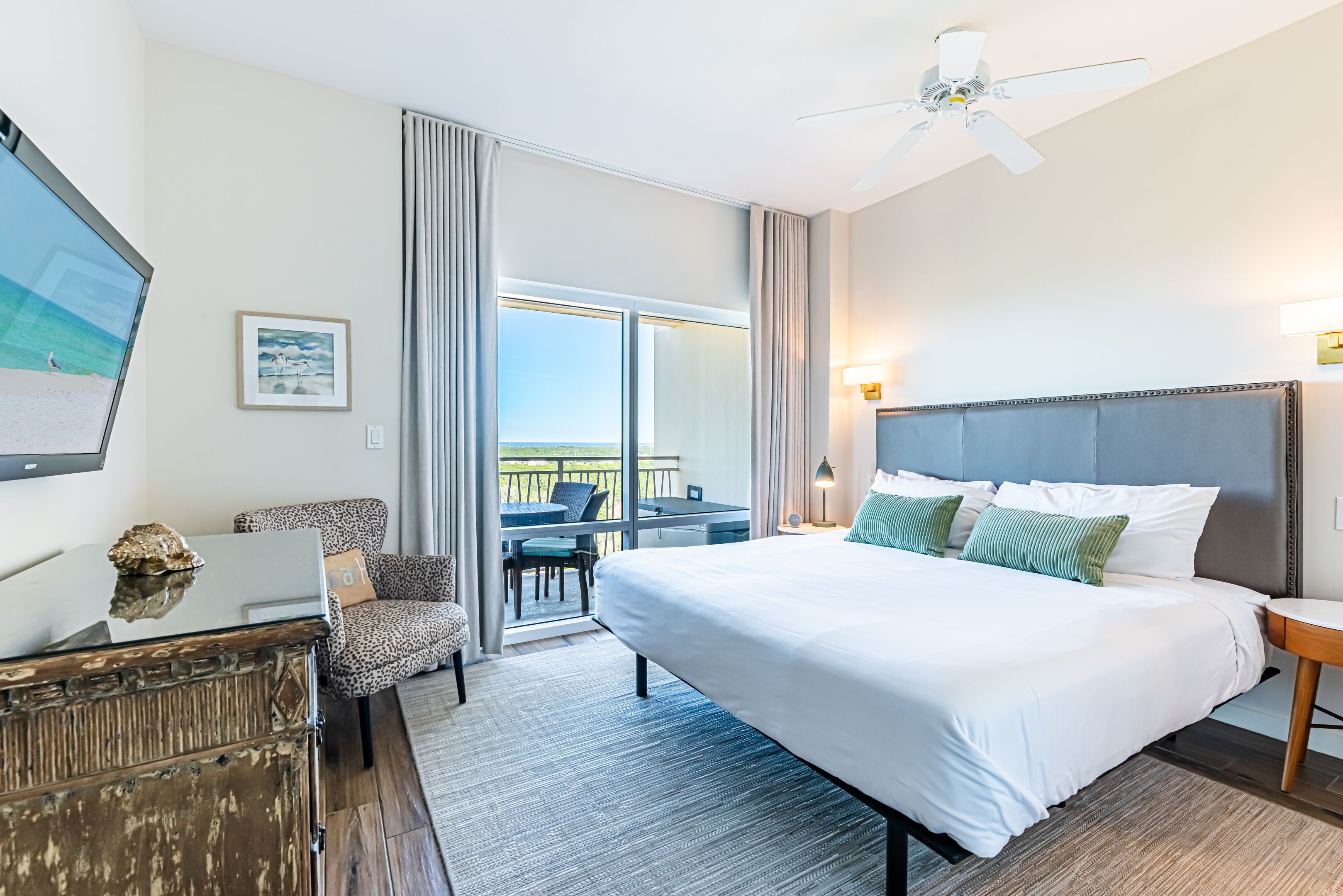 Habitación de hotel con una cama grande, un escritorio, una silla, un televisor y un balcón con vistas.