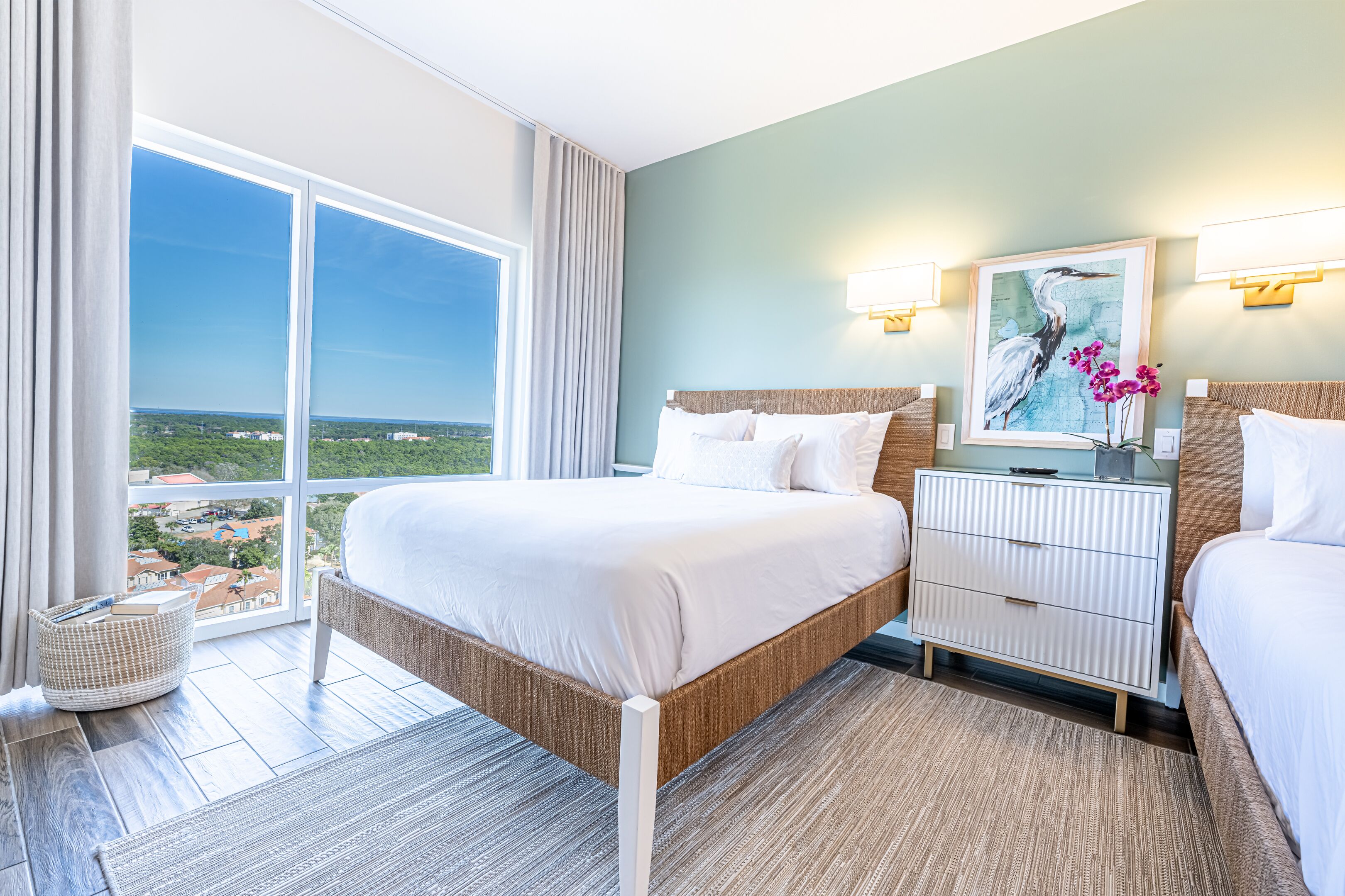 Quarto de hotel com uma cama grande, mesa de cabeceira, vista da cidade e janela com cortinas.