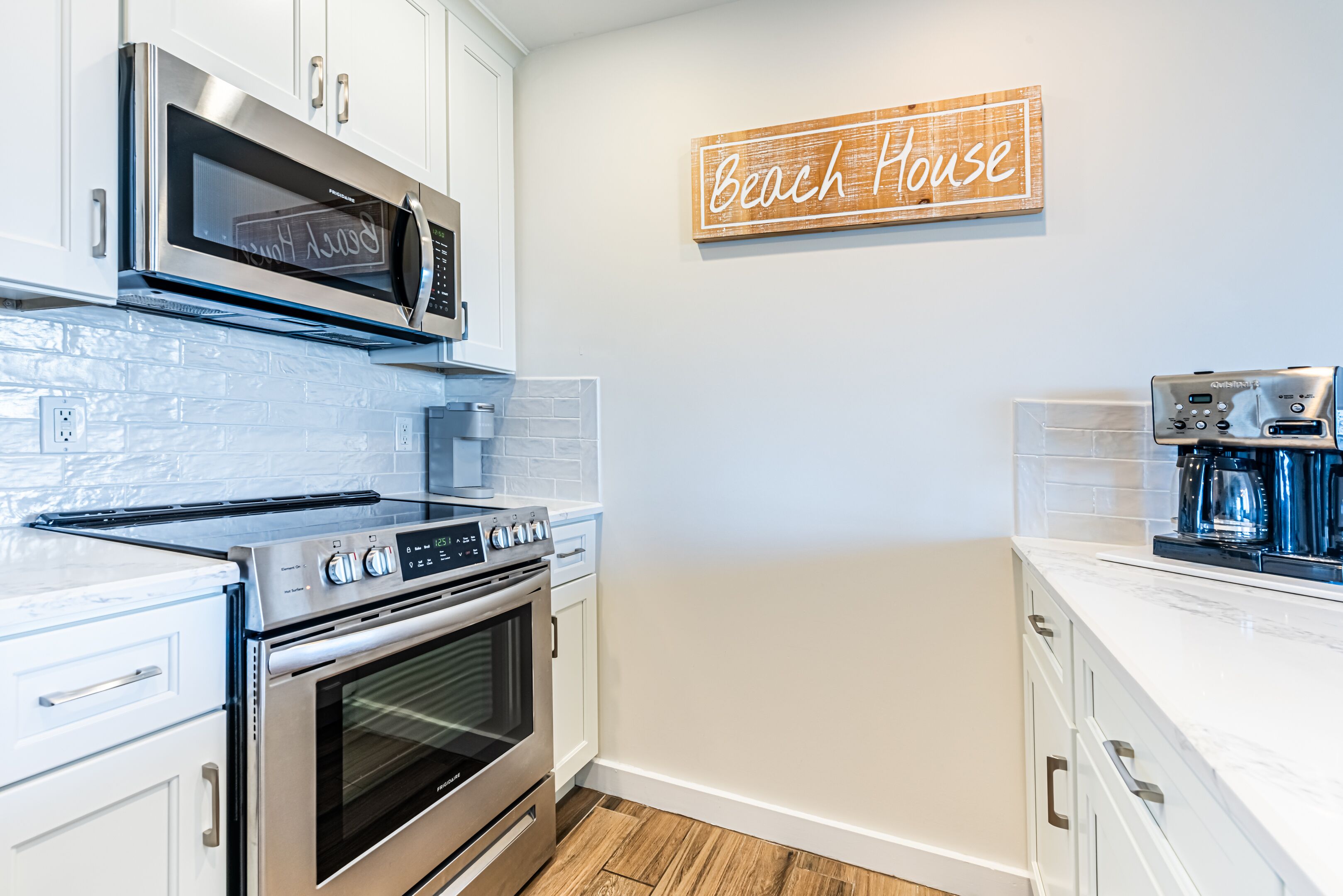 A kitchen with white cabinets, stainless steel appliances, and a wooden sign that reads "Beach House".