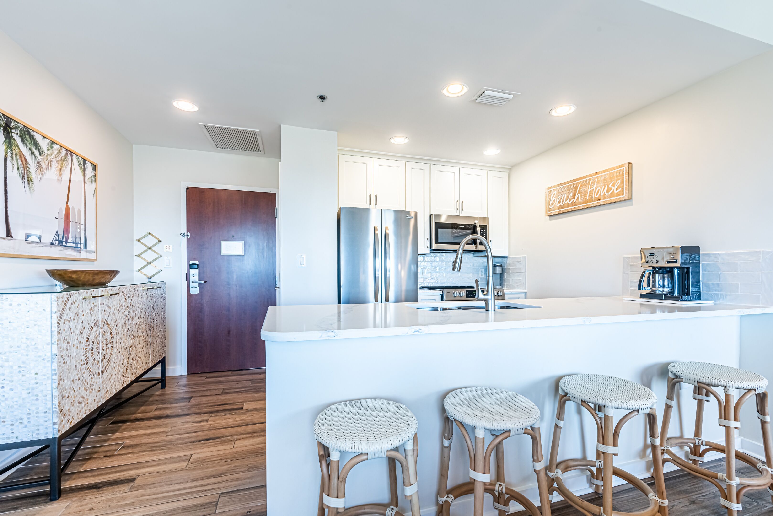A modern kitchen with white cabinets, stainless steel appliances, and a bar area with wicker stools.