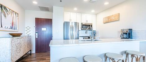 A modern kitchen with white cabinets, stainless steel appliances, and a bar area with wicker stools.
