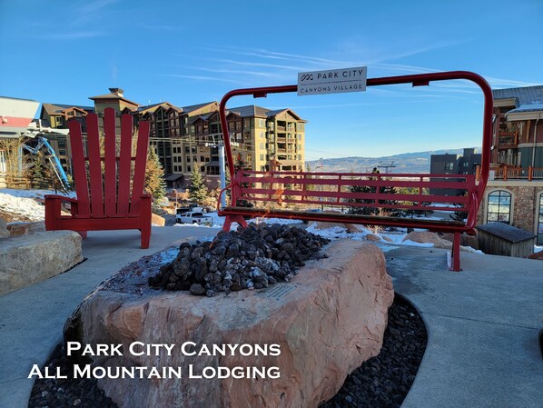 A red bench and chair in a snowy outdoor area with a view of a lodge and mountains.
