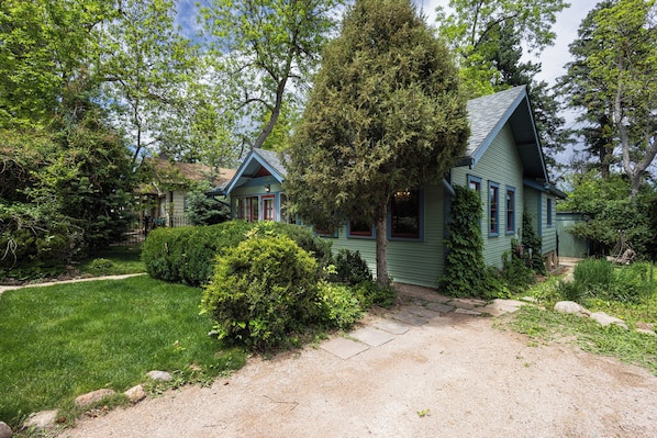 Une maison à deux étages, avec une façade verte, un chemin de pierre menant à la porte d’entrée et un jardin bien entretenu.