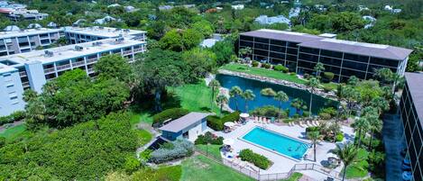 An aerial view of a hotel with a swimming pool, lush greenery, and multiple buildings.