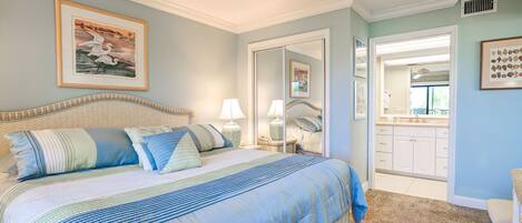 A bedroom with a large bed, a ceiling fan, a bathroom with a vanity, and a door leading to another room.