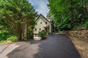 Set amidst lush greenery, this two-story house offers a secluded retreat with a gabled roof and a driveway.