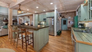 Une cuisine spacieuse avec un plancher en bois, des armoires vertes et un îlot central doté de tabourets de bar.