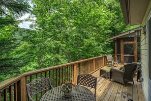 Relax on the deck with wicker chairs and a table, surrounded by lush greenery and trees.