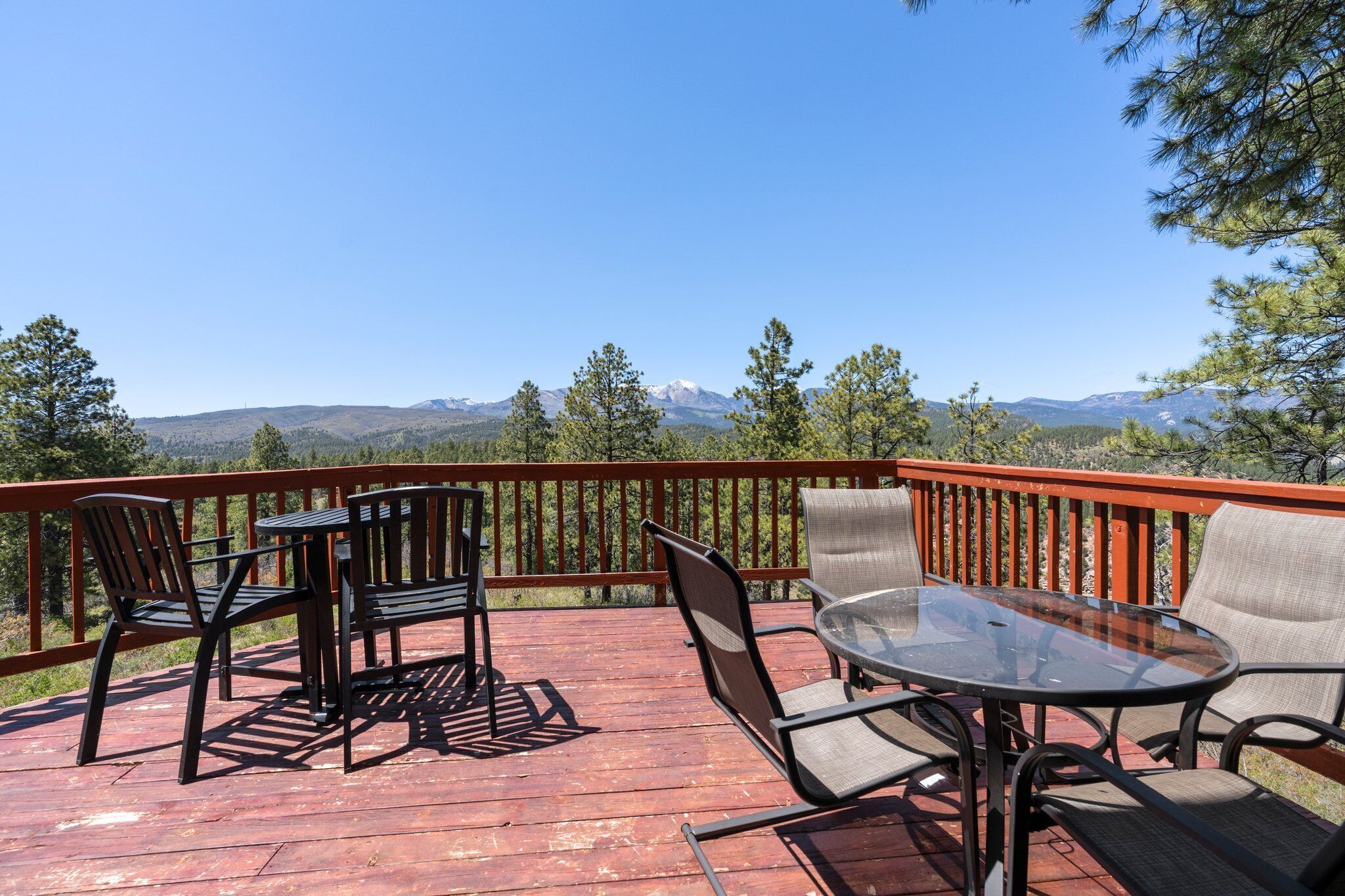A wooden deck with outdoor furniture, a glass table, and a view of mountains.