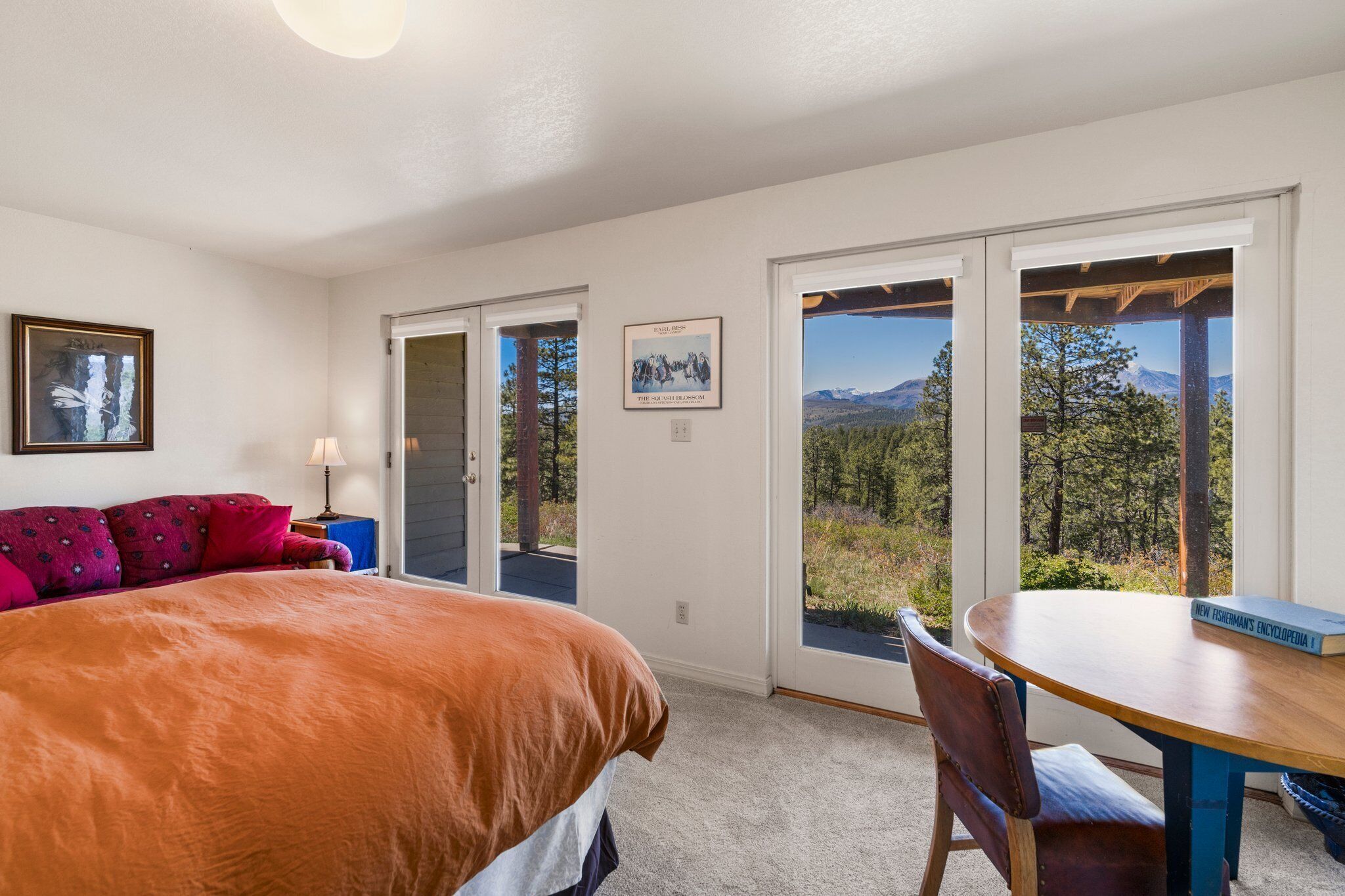 A bedroom with a large bed, a wooden table, and a view of a mountainous landscape through the door.