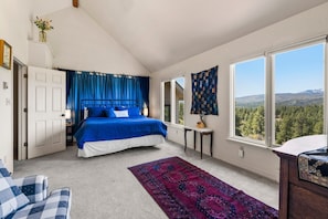 Relax in this serene bedroom with a large bed, sloped ceiling, and breathtaking mountain views through the large window.