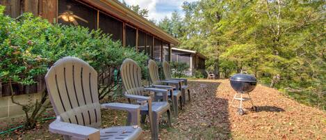 A row of Adirondack chairs outside a building with a covered patio area and a barbecue grill.