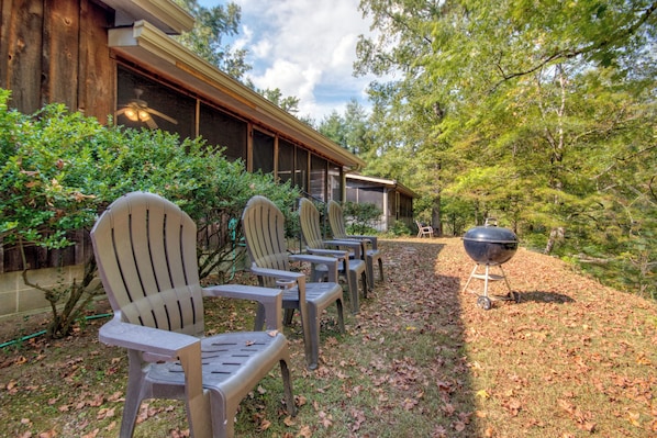 A row of Adirondack chairs outside a building with a covered patio area and a barbecue grill.