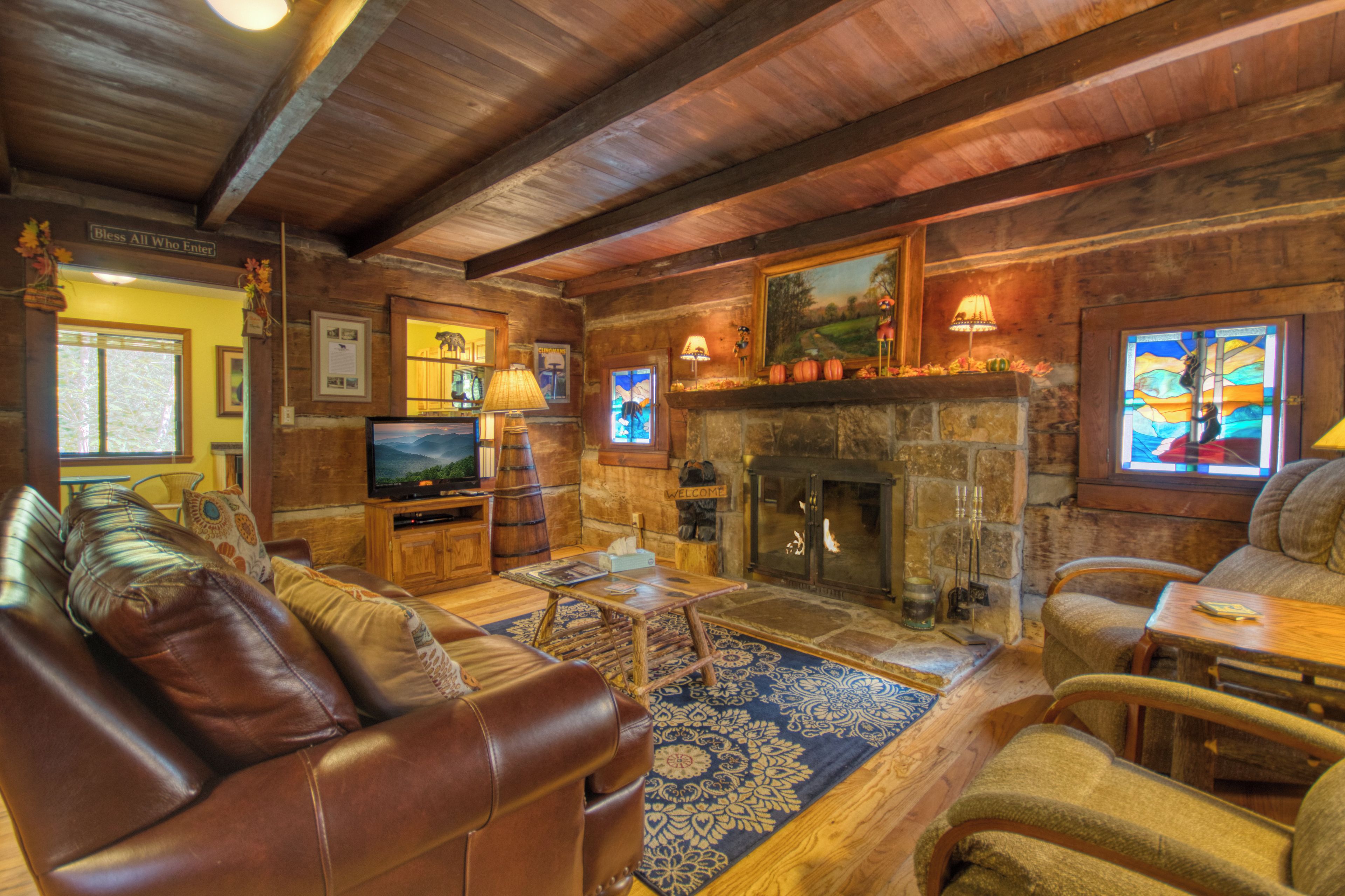 A cozy living room with leather sofas, a fireplace, wooden beams, and a television.