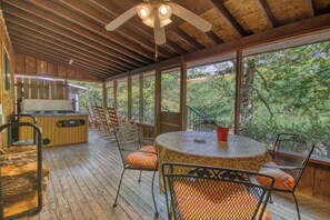 A covered outdoor area with a wooden deck, a round table with chairs, and a hot tub.