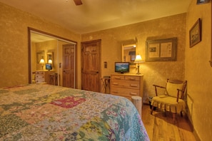 A bedroom with a floral bedspread, wooden furniture, a television, and a mirror on the wall.