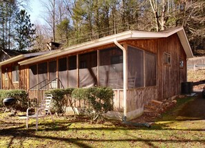 A rustic wooden cabin with a covered porch, a grill, and a small garden area. - Historic Riverside Cabin w/Hot Tub in Gatinburg (GATLINBURG)