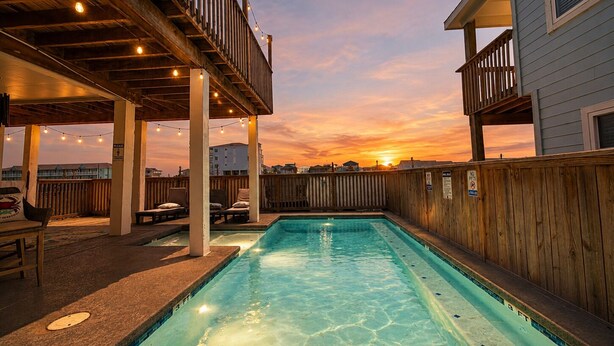 Ein Pool mit Holzterrasse, Liegestühlen und Lichterkette.