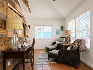 Una habitación acogedora con pared de madera, una mesa de comedor con sillas, un sofá de mimbre, una mesita auxiliar pequeña y una ventana con persianas.