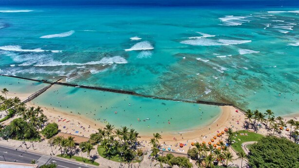 An aerial view of a beach with clear turquoise waters, a sandy shore, and palm trees. - Spectacular Diamond Head and Ocean Views! Free Valet Parking, Wi-Fi, Pool! (Honolulu)