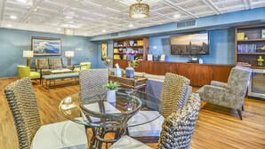 A spacious lobby with a high ceiling, a seating area with a round glass table, and a bookshelf filled with books. - Spectacular Diamond Head and Ocean Views! Free Valet Parking, Wi-Fi, Pool! (Honolulu)