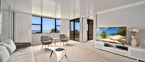 A modern living room with a large TV, comfortable seating, and a view of the ocean.