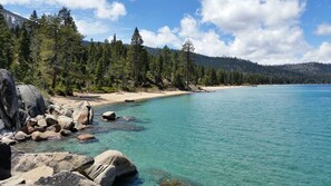 A clear turquoise lake with a sandy beach and large rocks in the foreground.