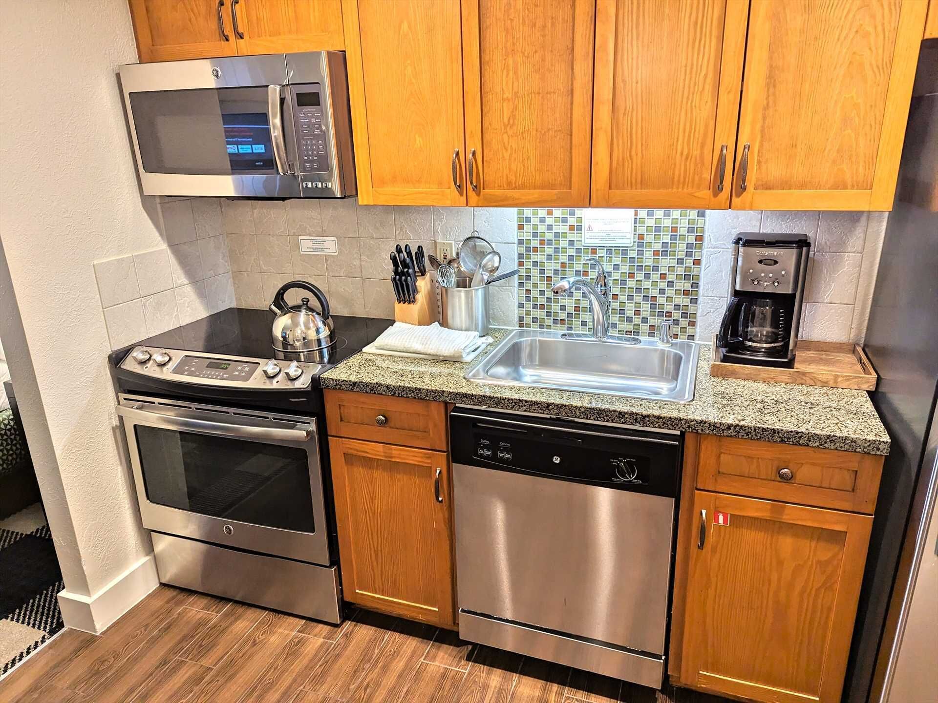 A modern kitchen with stainless steel appliances, wooden cabinets, a granite countertop, and a coffee maker.
