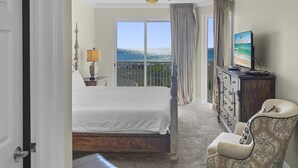 Een hotelkamer met een bed, een stoel, een dressoir, een televisie en een balkon met uitzicht.