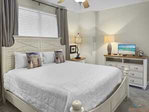 Une chambre à coucher bien rangée, avec un grand lit, une table de chevet, un téléviseur et un bureau avec des tiroirs.