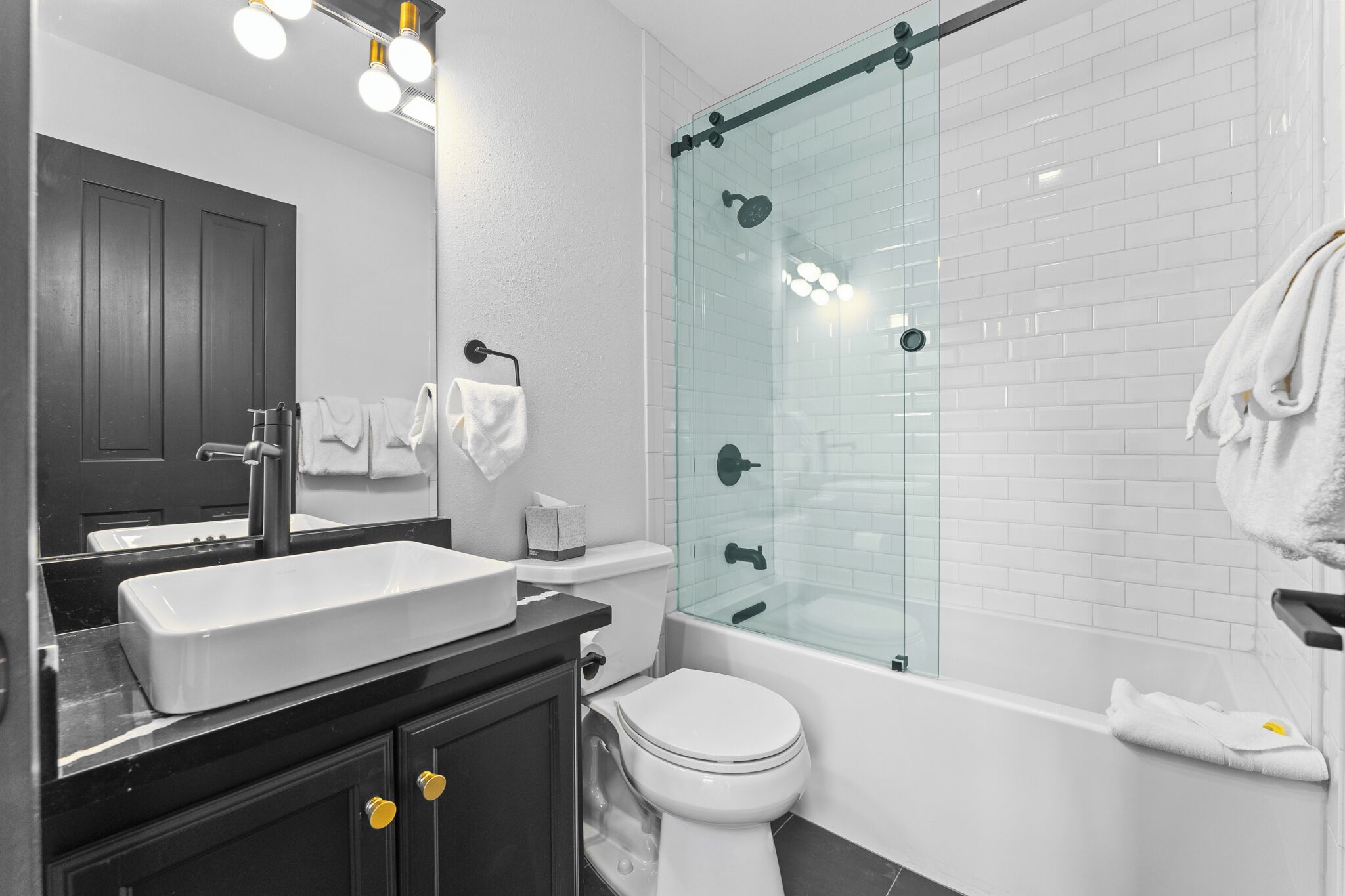 A modern bathroom with a glass-enclosed shower, a white sink, and a dark vanity.