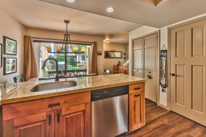 A kitchen with a granite countertop, stainless steel dishwasher, wooden cabinets, and a large window with curtains. - Luxury Condo, Private Hot Tub & Year-Round Recreation at Park City Racquet Club (Park City)