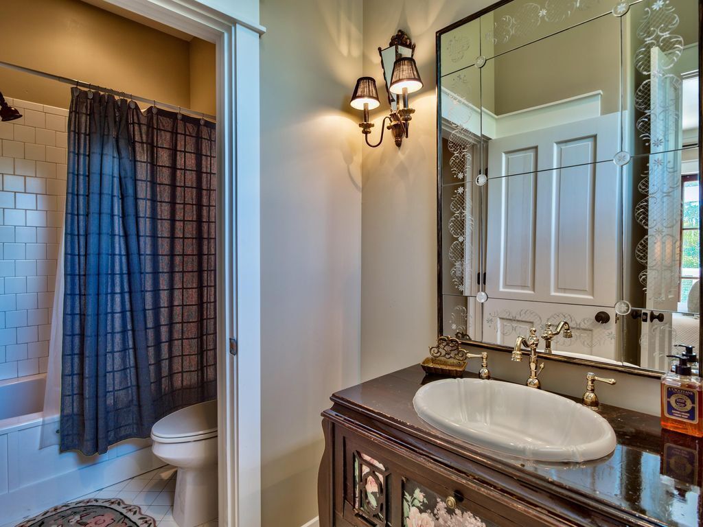 A bathroom with a white toilet, a dark blue shower curtain, a white sink with a mirror above it, and a decorative cabinet below.