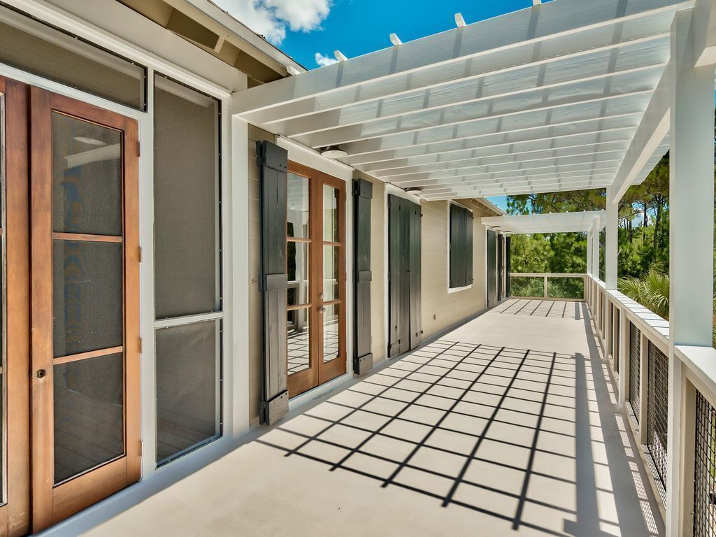 A covered outdoor area with a grid floor, sliding glass doors, and a pergola structure.