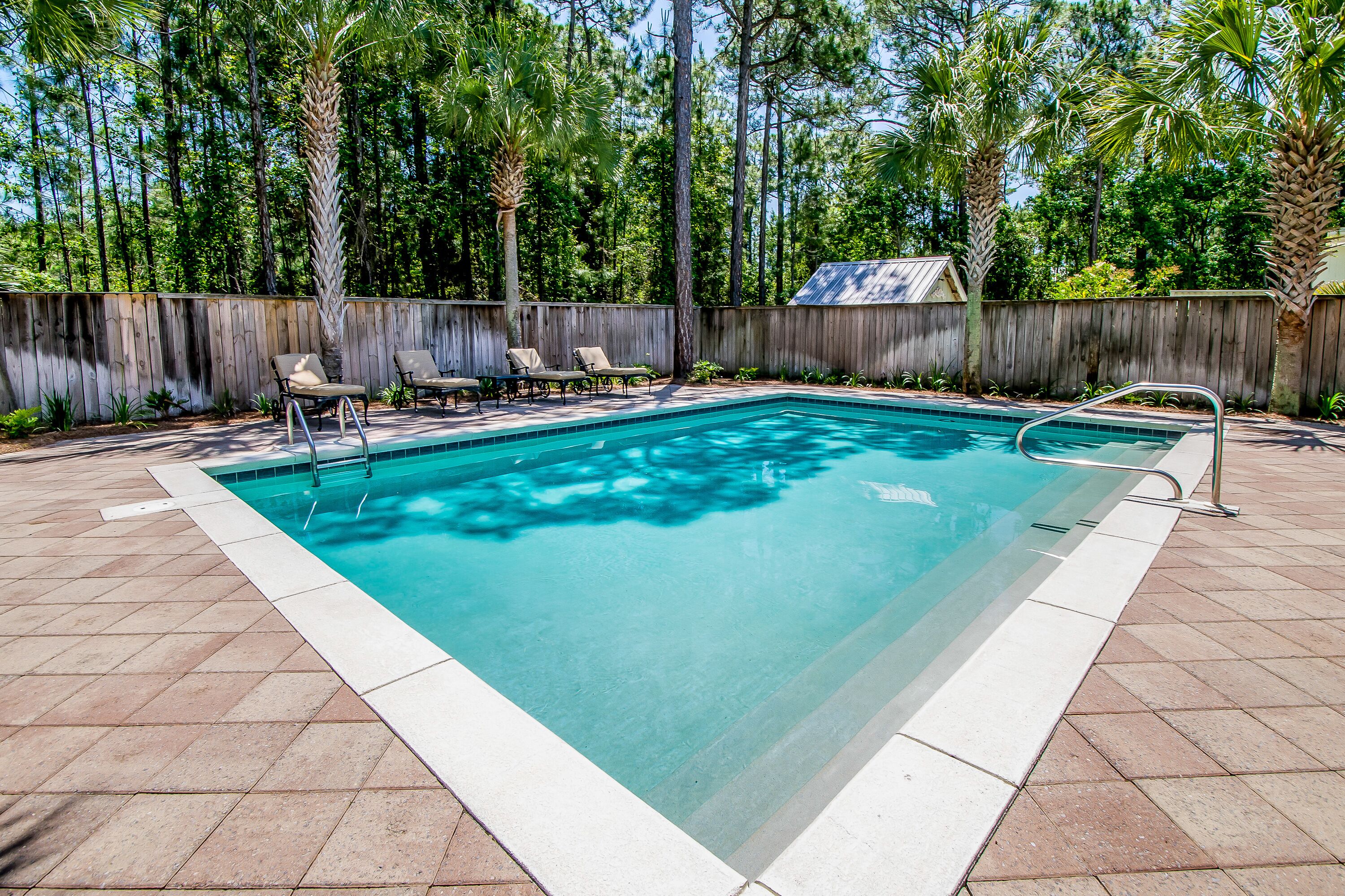 A rectangular swimming pool with a wooden fence and palm trees in the background.
