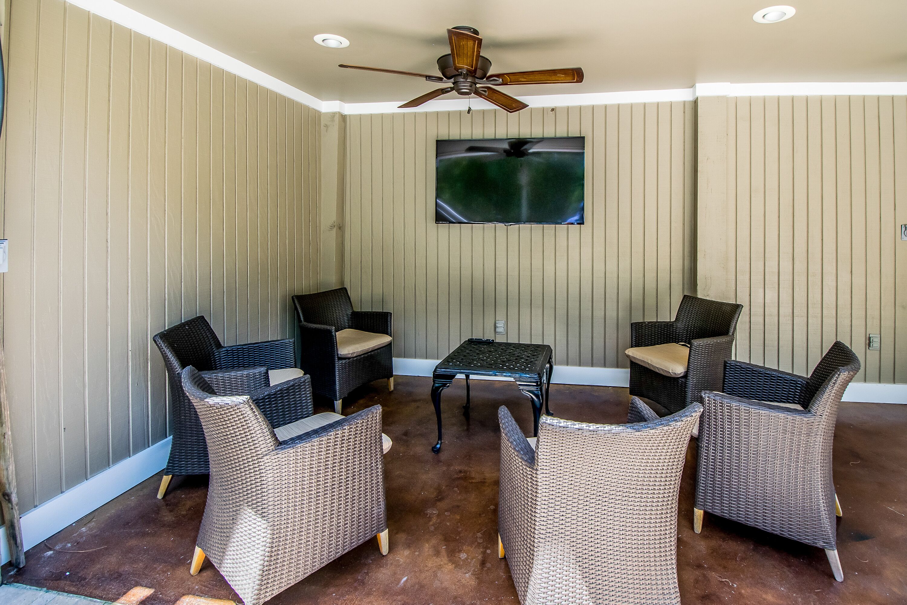 A covered patio area with wicker furniture, a ceiling fan, and a mounted TV.