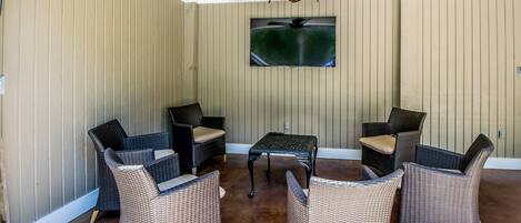 A covered patio area with wicker furniture, a ceiling fan, and a mounted TV.