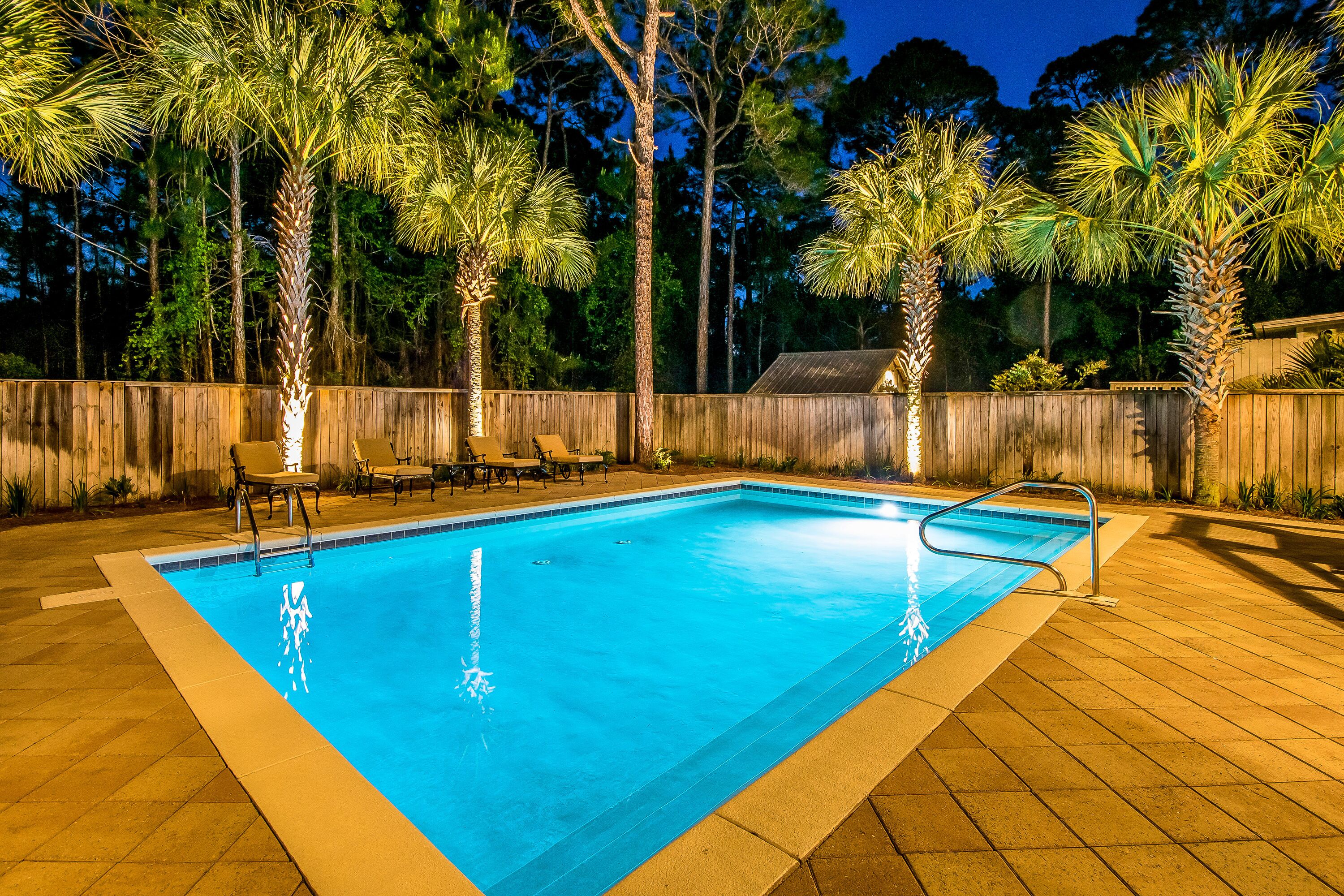 A rectangular swimming pool with a wooden deck surrounding it, equipped with a metal ladder and a few lounge chairs.