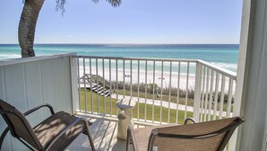Un balcon avec deux fauteuils en osier, une petite table et une vue sur la plage et l’océan.