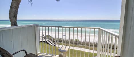 A balcony with two wicker chairs, a small table, and a view of the beach and ocean.