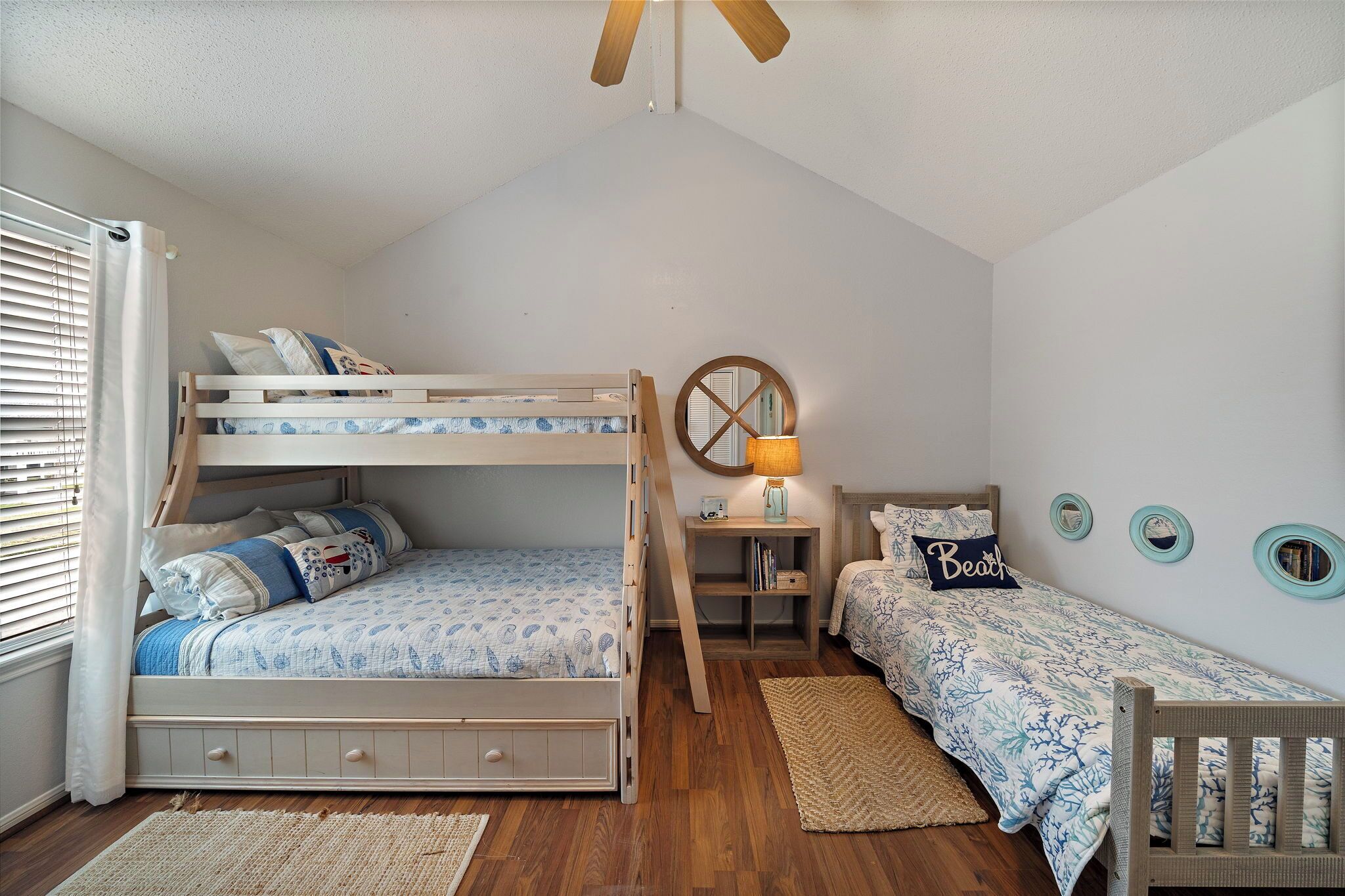 A bedroom with a bunk bed, a desk with a lamp, a small chair, and a crib.