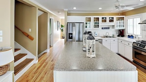 A modern kitchen with a central island, stainless steel appliances, and a view to the dining area. - Sandys North Shore | Pet Friendly, Large Deck! (Tybee Island)