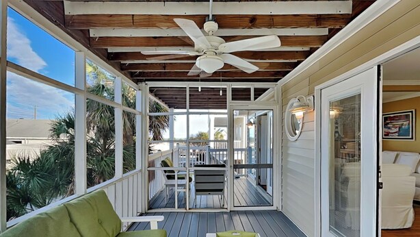 A covered porch with a green sofa, a small table, and a ceiling fan. - Sandys North Shore | Pet Friendly, Large Deck! (Tybee Island)