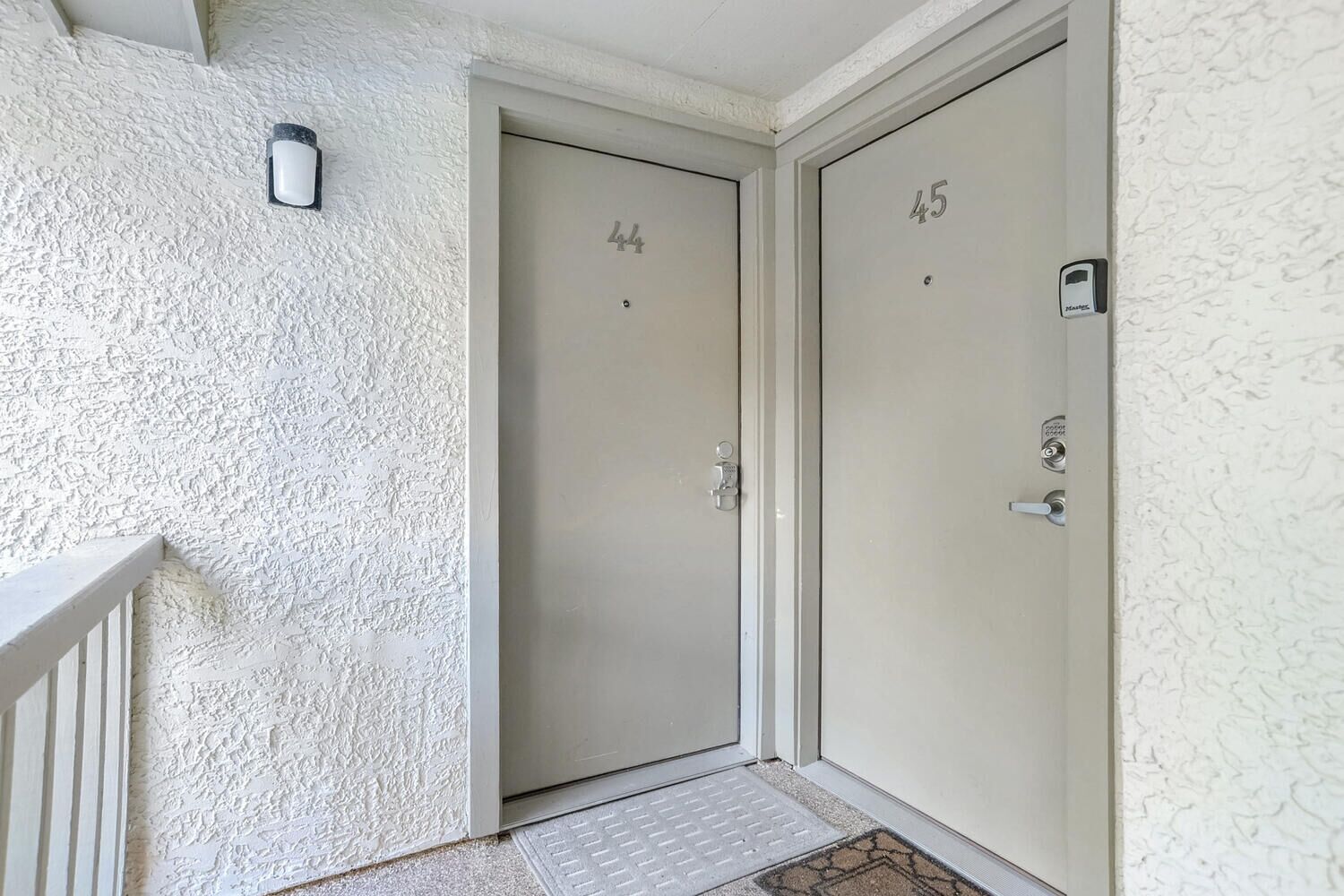 Dos puertas con los números 44 y 45, un escalón pequeño que lleva a la entrada, y una pared con textura.