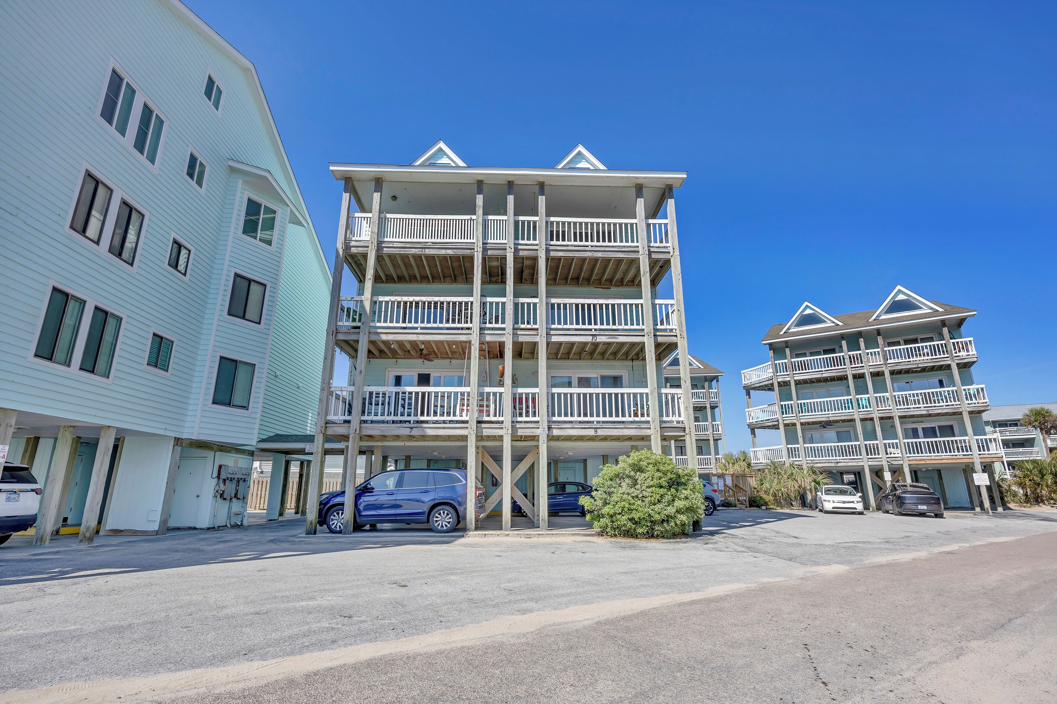 A multi-story hotel with balconies, a parking area, and a clear sky.