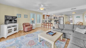 A living room with a TV, sofa, coffee table, patterned rug, and a ceiling fan.
