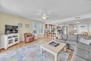 A living room with a TV, sofa, coffee table, patterned rug, and a ceiling fan.