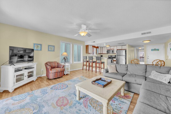 A living room with a TV, sofa, coffee table, patterned rug, and a ceiling fan.