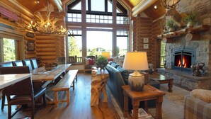 L’intérieur d’une cabane en rondins, avec une grande cheminée en pierre, des meubles en bois et un lustre.